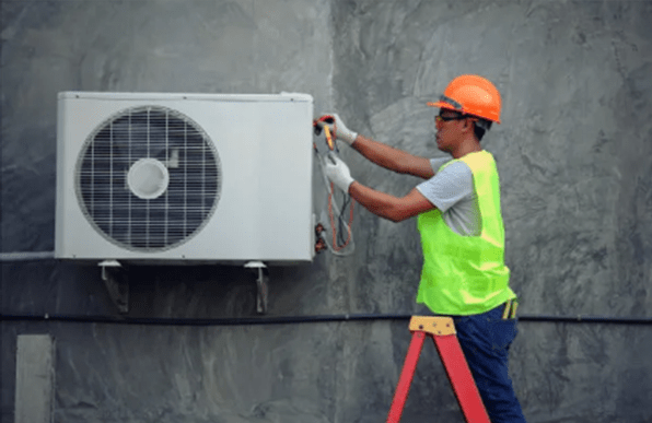 A technician standing on a ladder overhauling an air conditioner compressor